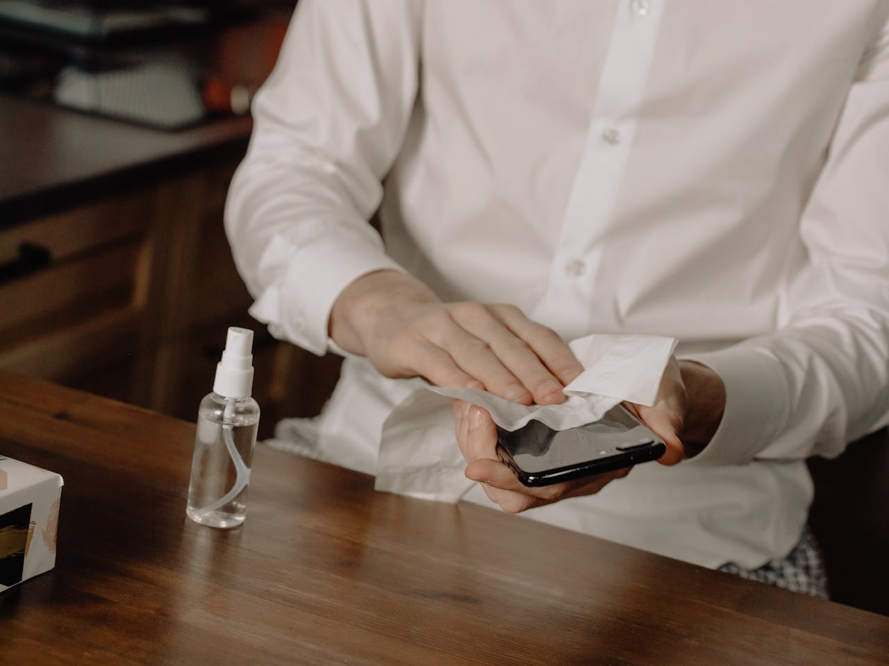 A person sanitizes their smartphone at a table, promoting healthy hygiene in home settings.